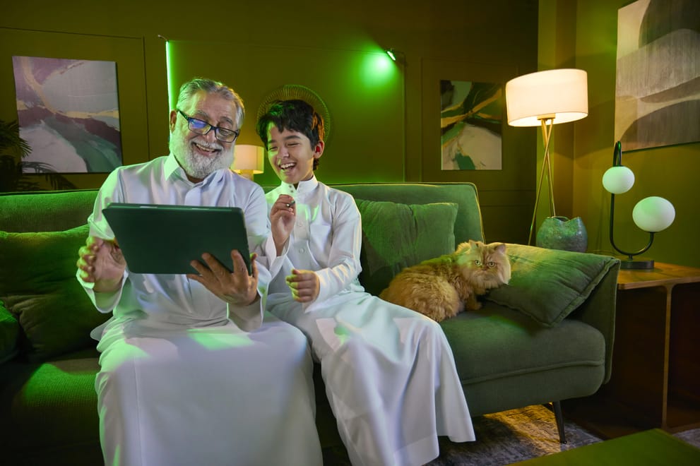 Grandfather and grandson using a tablet at home on Salam postpaid and roaming packages in Saudi Arabia